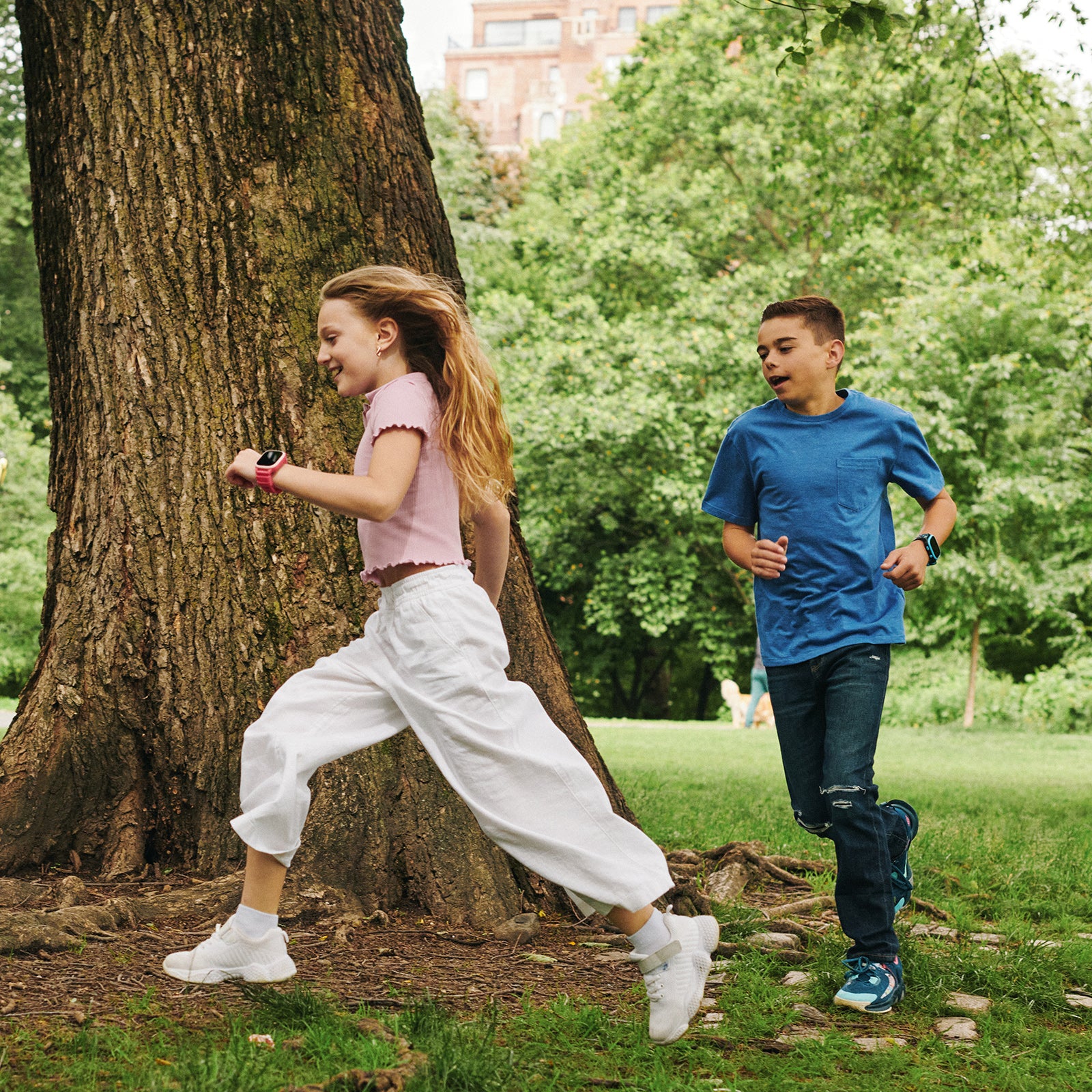 Two children running in a park with trees and greenery in the background