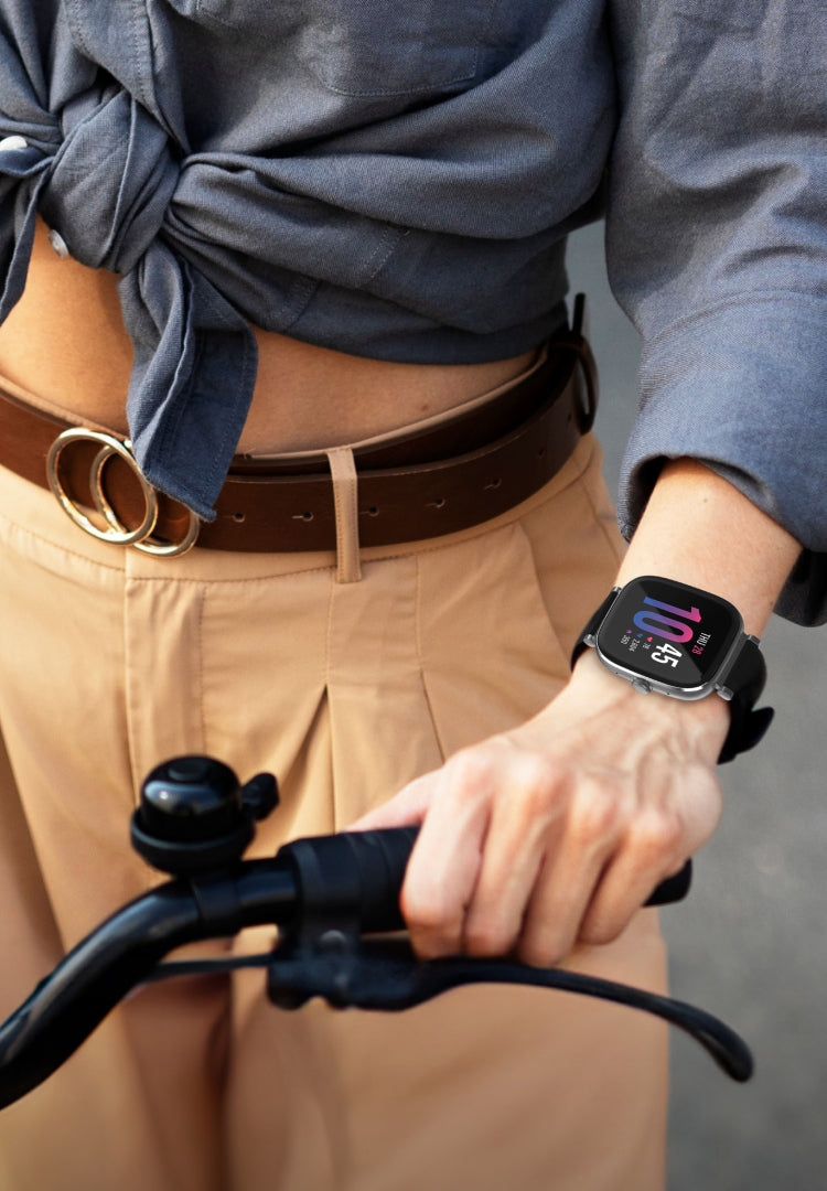 Person holding bicycle handlebars with a smartwatch on wrist, wearing a blue shirt and beige pants.